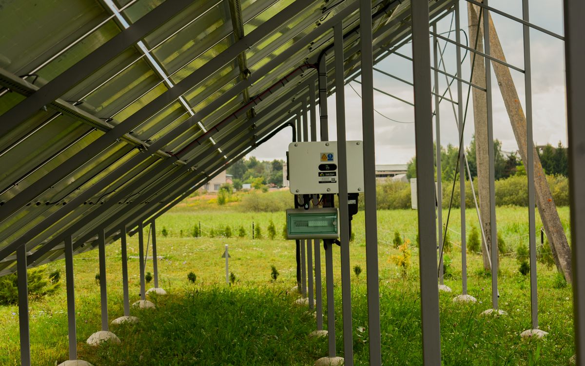 Electrical metering panel beside a greenhouse structure with solar panels visible on an adjacent roof